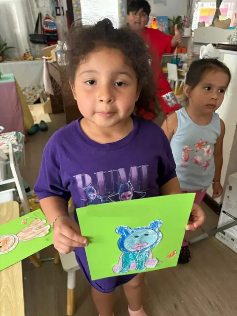A girl holds up her colored lion craft on green paper