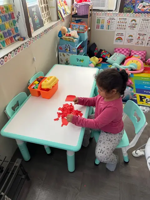 A preschooler tears red paper for a collage at the craft table
