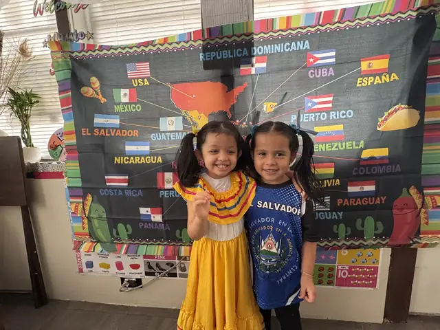 Two smiling girls hug in front of the flags map